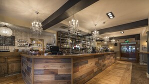 A bar area with wooden flooring, a central bar counter, and multiple chandeliers. - The Golden Lion Hotel, St Ives, Cambridgeshire (St Ives)