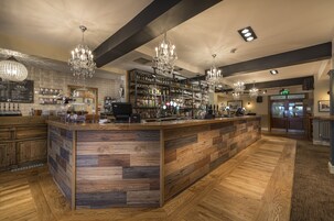Uma área de bar com piso de madeira, um balcão central e vários candelabros.