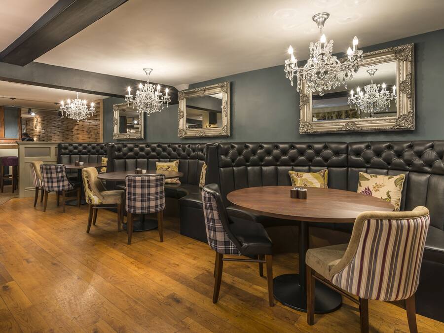 A restaurant with a dark wood floor, leather booth seating, and chandeliers.