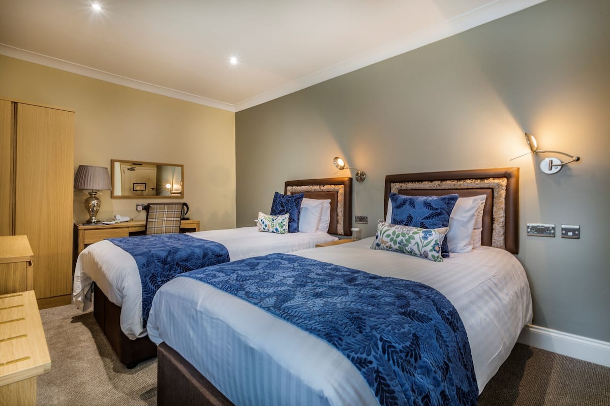 Une chambre d’hôtel avec deux lits, un bureau, une chaise, une lampe, un miroir et un luminaire fixé au mur.