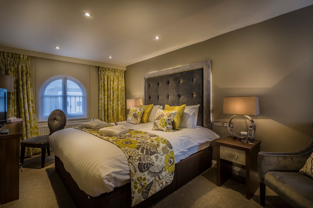 Une chambre d’hôtel avec un grand lit, deux tables de chevet, une chaise, un bureau et une fenêtre avec des rideaux.