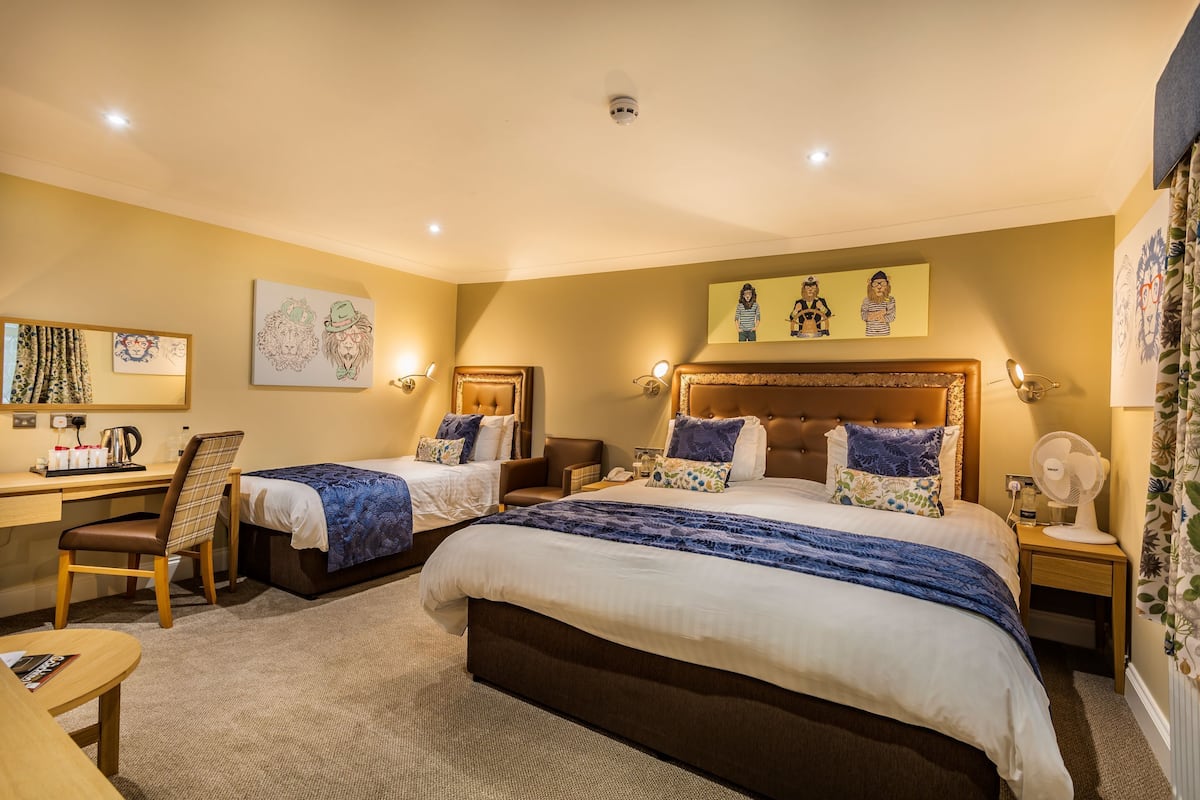 Une chambre d’hôtel avec deux lits, un bureau et une chaise. Elle est équipée de lampes murales et d’un ventilateur de plafond.