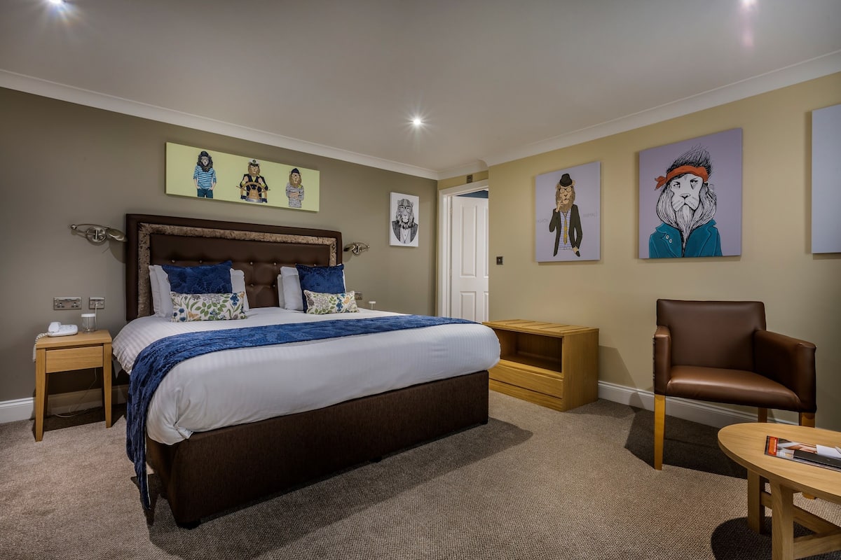 Une chambre d’hôtel avec un grand lit, deux tables de chevet, une chaise et des œuvres d’art accrochées aux murs.