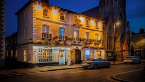 A historic building with a restaurant and coffee house on the ground floor, a balcony with flowers, and a clock tower in the background. - The Golden Lion Hotel, St Ives, Cambridgeshire (St Ives)