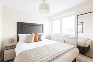 Un dormitorio moderno con una cama grande, una mesita de noche, una lámpara de noche, un ventanal con vistas y un espejo.