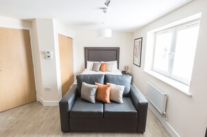 Un dormitorio moderno con una cama, un sofá oscuro y una ventana que proporciona luz natural.