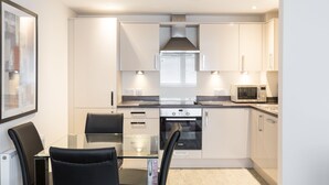 A modern kitchen with white cabinets, a glass dining table, black chairs, and built-in appliances.