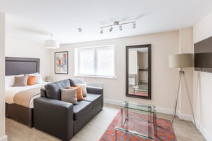 Un dormitorio moderno con cama, sofá gris y una mesa de centro de cristal.