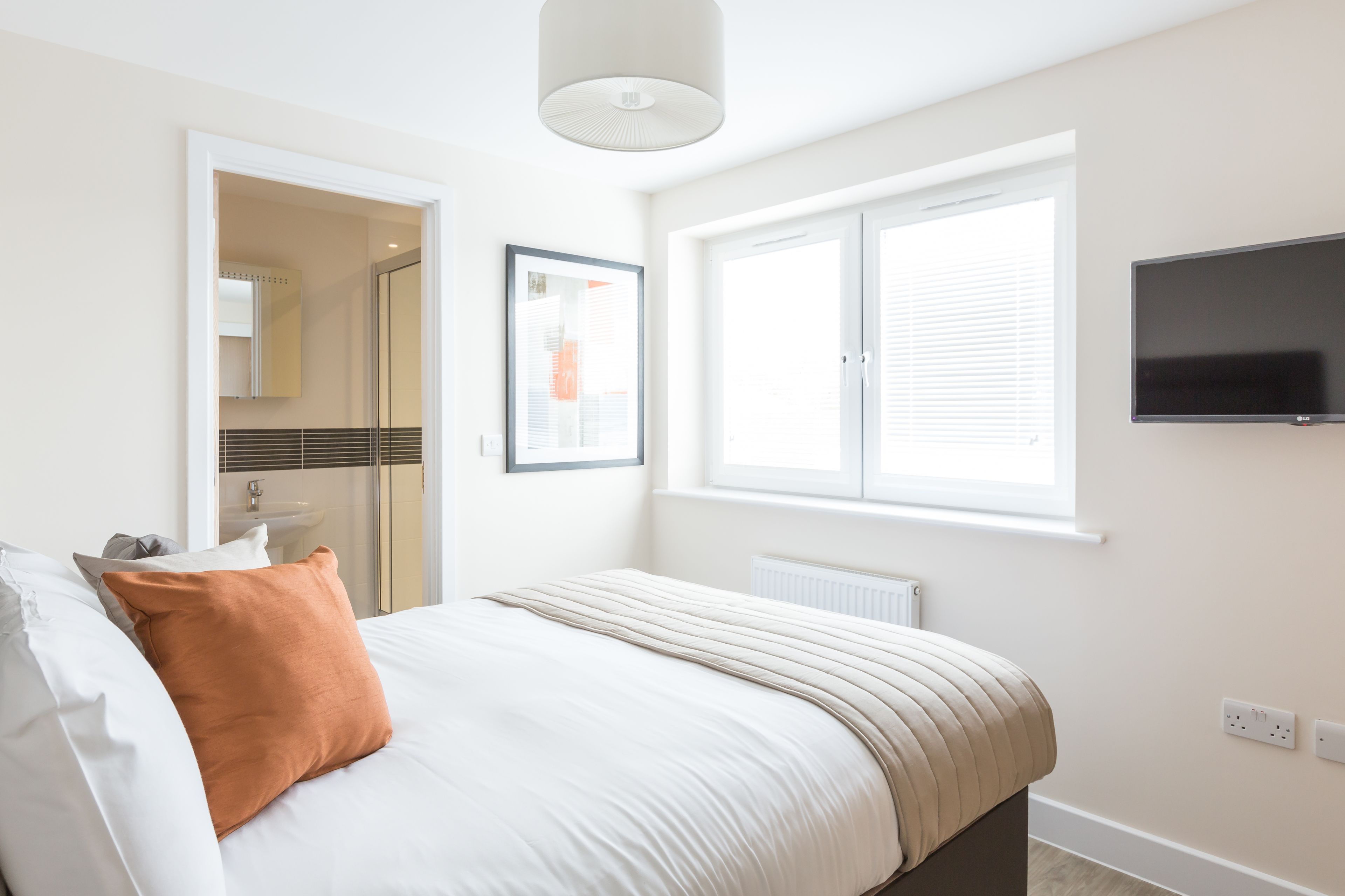 A bedroom with a bed, a TV, a window, and a door leading to a bathroom.