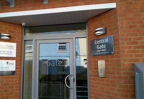 Entrada de un hotel con puerta de cristal, un cartel que dice Central Gate y otro indicando el uso de apartamentos para pescadores.