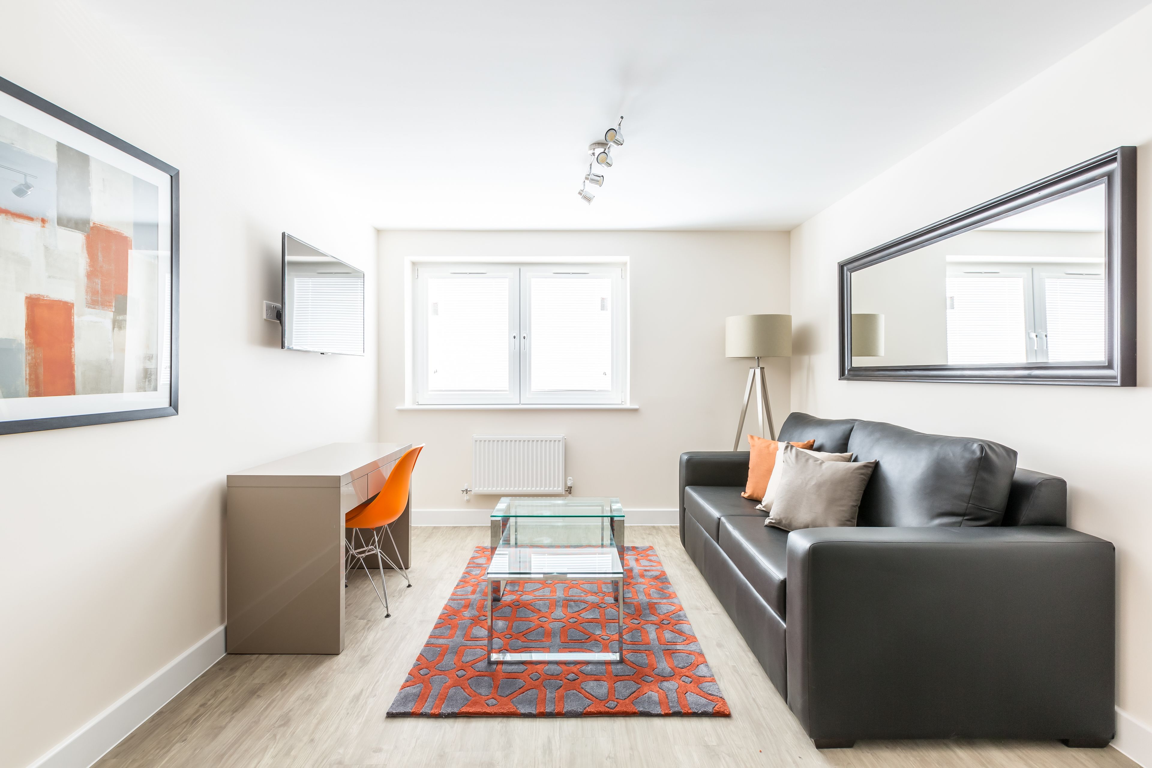 A modern living room with a glass coffee table, a black leather sofa, and a patterned rug.