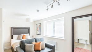 A modern bedroom with a bed, a sofa, a large mirror, and a window with blinds.