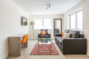A modern living room with a glass coffee table, a sofa, a desk, and an orange chair.