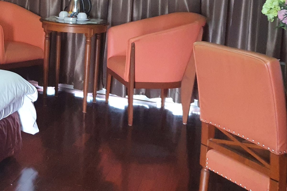 A hotel room with a large bed, two chairs, a small table with a lamp, and a telephone.