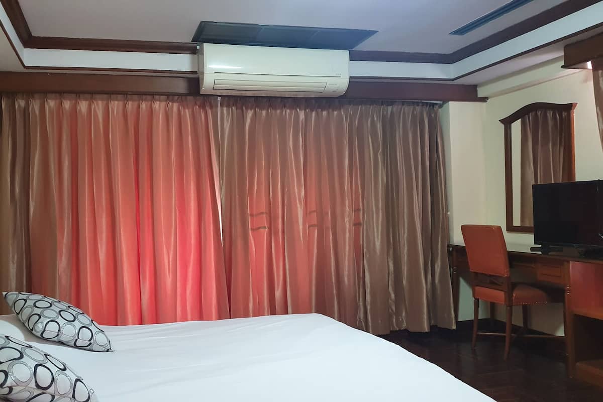 A hotel room with a bed, two pillows, a desk with a chair, a television, and an air conditioning unit.