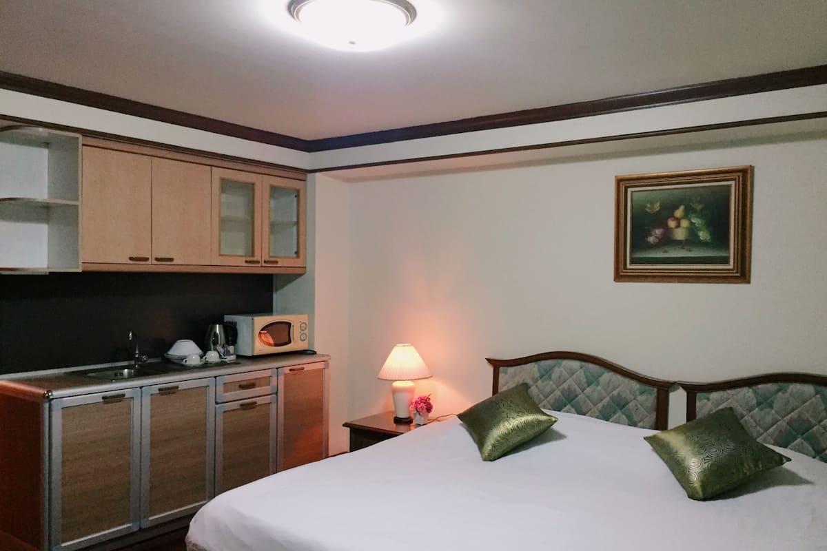 A hotel room with a bed, a nightstand with a lamp, a microwave, and wooden cabinets.