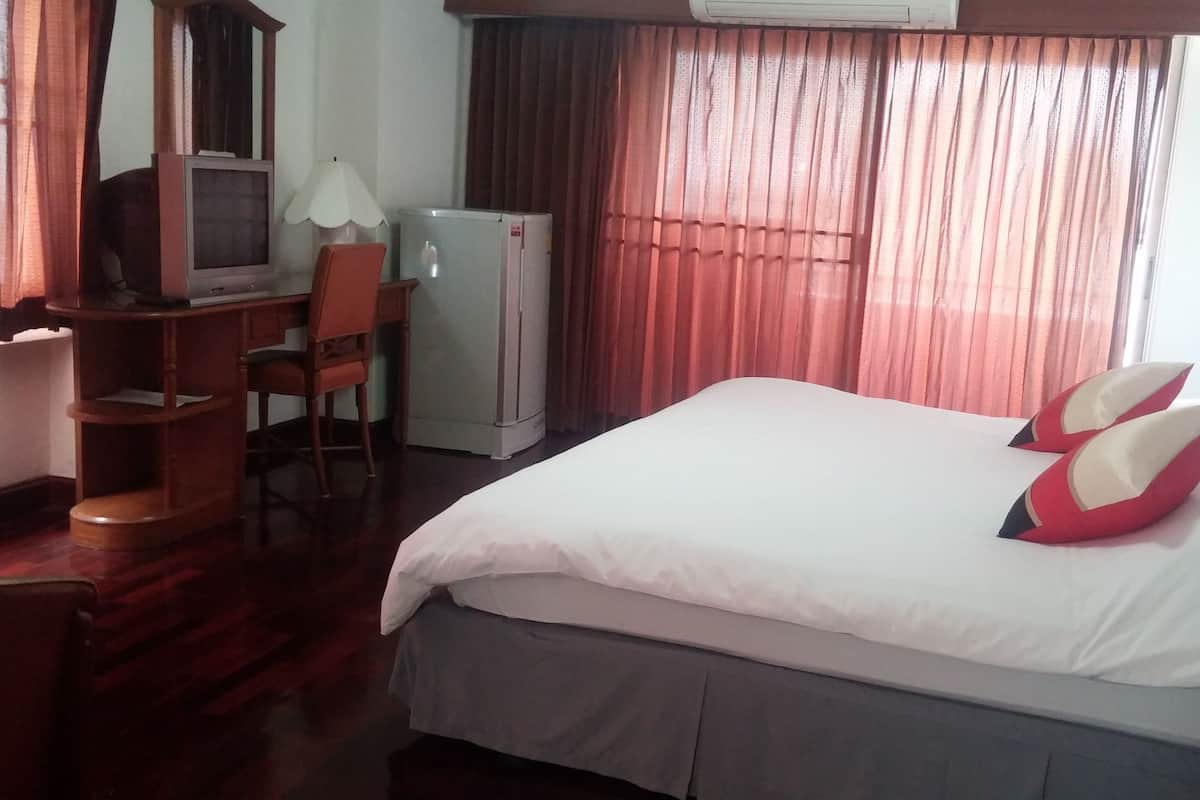 A hotel room with a bed, a desk with a chair, a television, and a refrigerator.