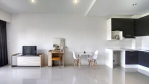 Een moderne, minimalistische woonkamer met een flatscreen televisie, een bureau met stoel, en een eethoek met tafel en stoelen.