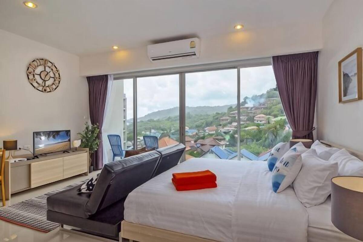 A hotel room with a large bed, a TV, a desk, and a view of a cityscape.