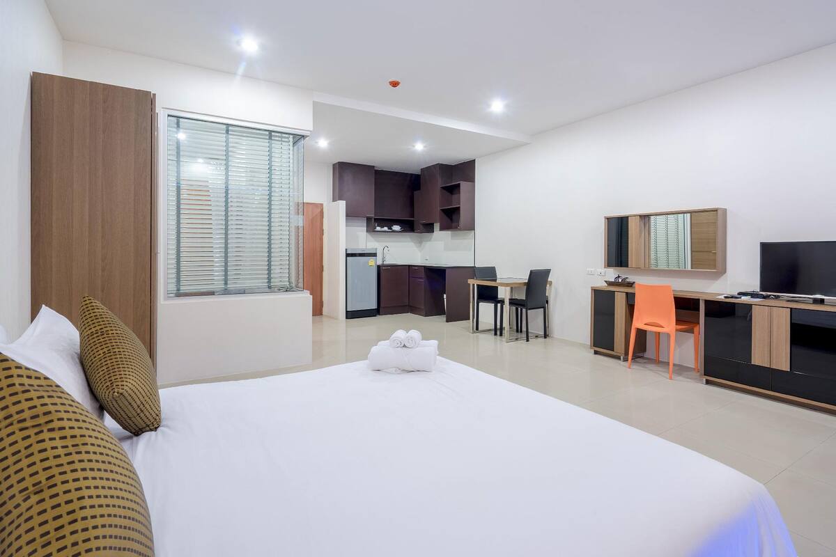 A hotel room with a bed, a desk, a chair, a TV, and a kitchenette.