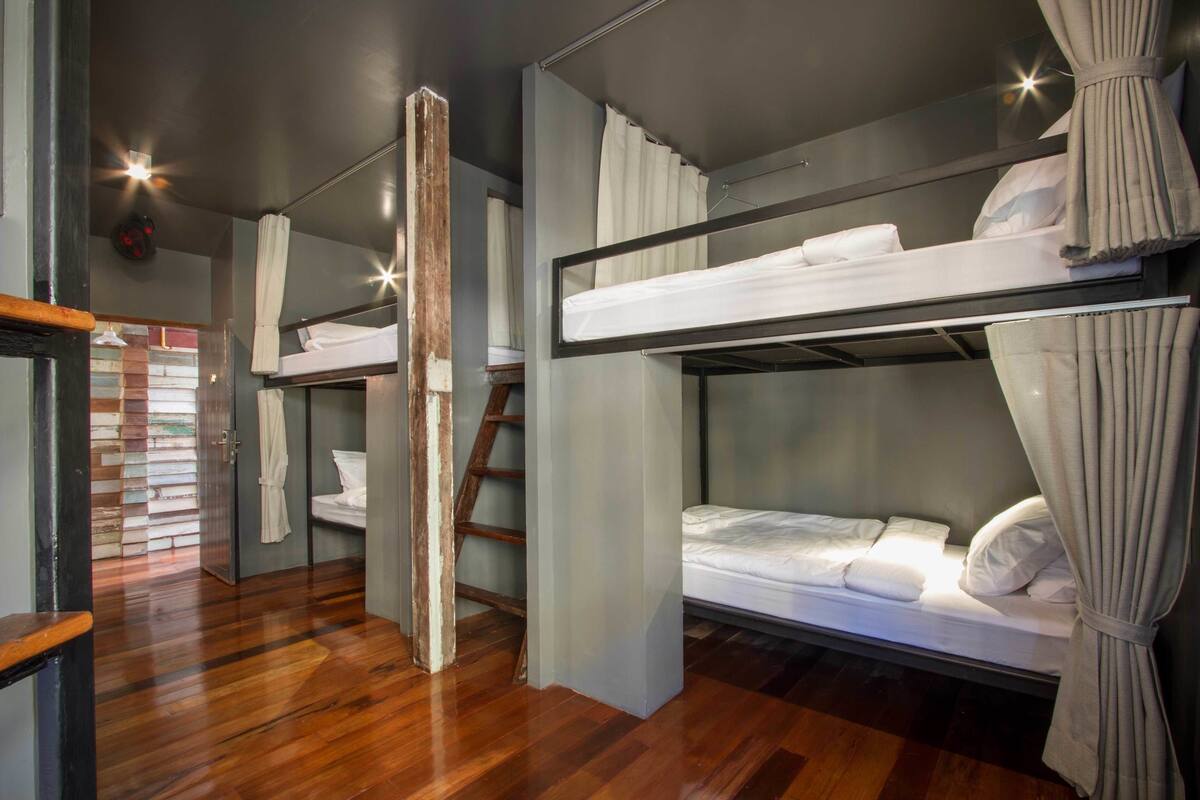 A bunk bed room with wooden flooring, a ladder, and curtains.