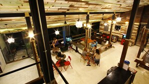 A spacious restaurant with high ceilings and exposed wooden beams. There are multiple dining tables and chairs, and the space is well-lit with hanging pendant lights. - Here Hostel (Bangkok)