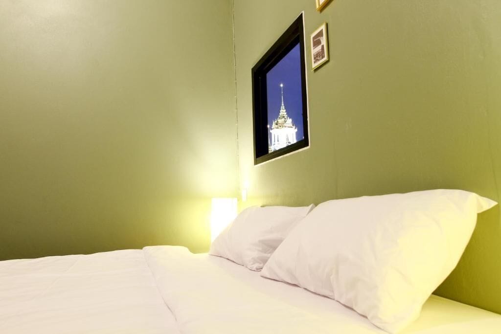 A room with a bed, a framed picture on the wall, and a window with a view of a building.