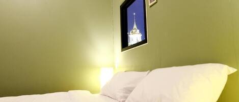 A room with a bed, a framed picture on the wall, and a window with a view of a building.