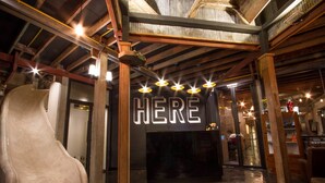 An indoor space with a large, curved white chair, wooden beams, and a sign that reads "HERE". - Here Hostel (Bangkok)