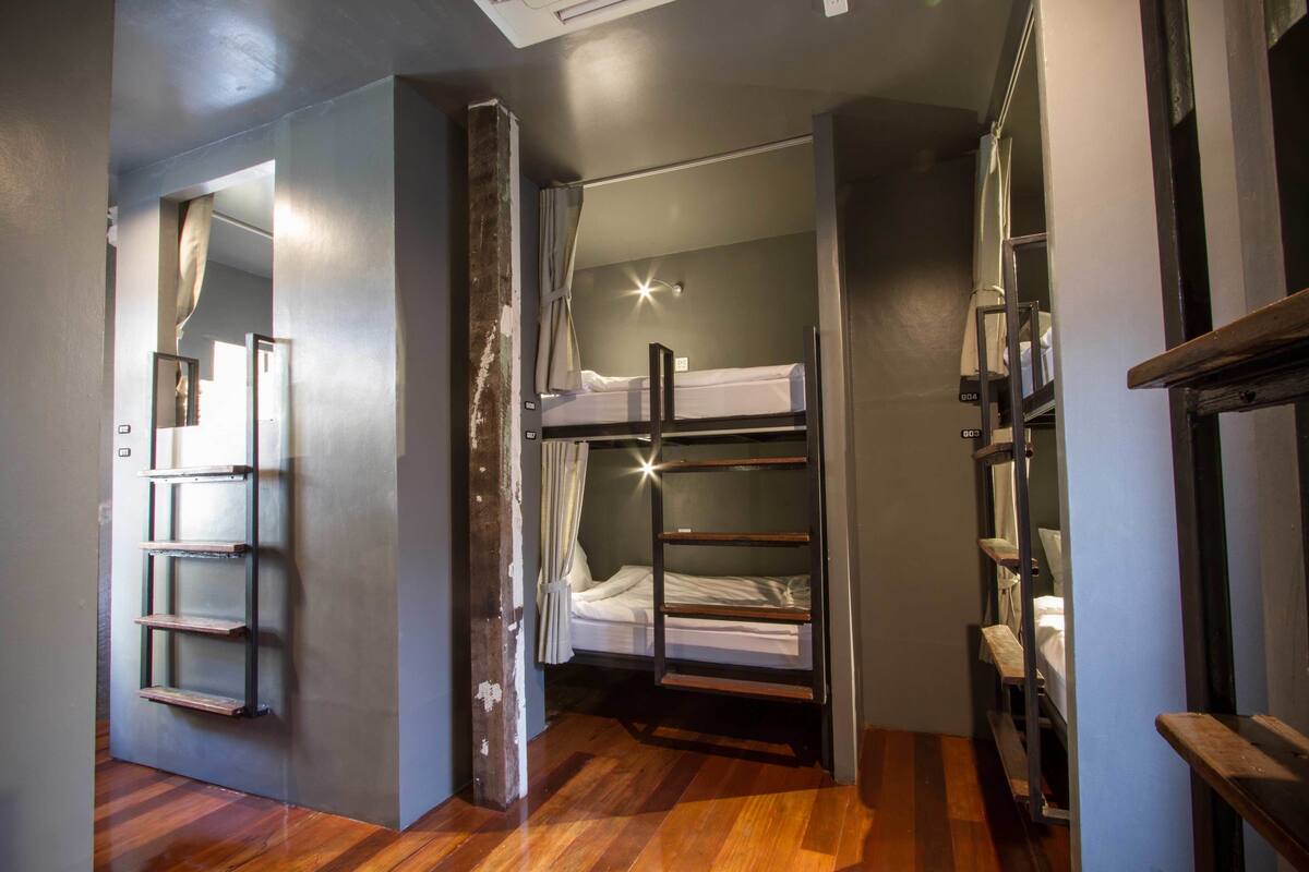 A compact room with a bunk bed, a wooden ladder, and a small shelf unit.