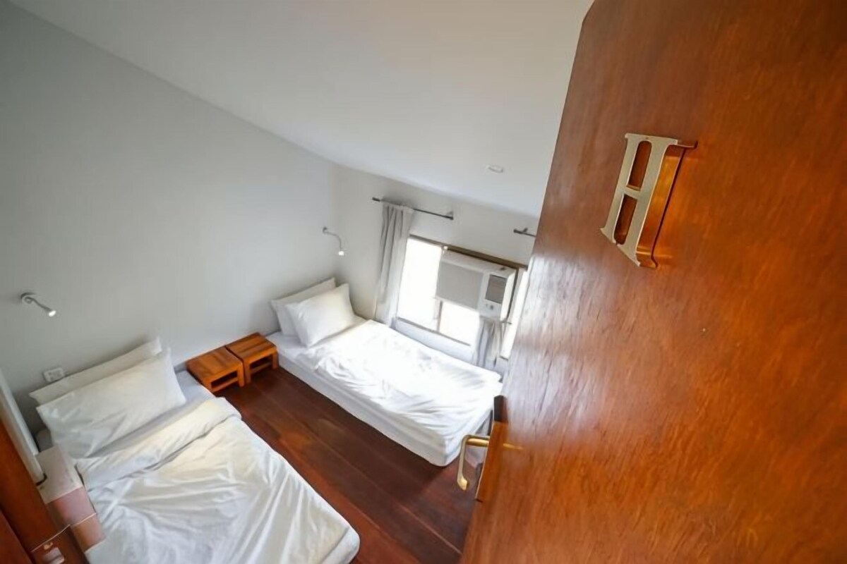 A bedroom with two beds, a wooden floor, a window, and a door with a handle.
