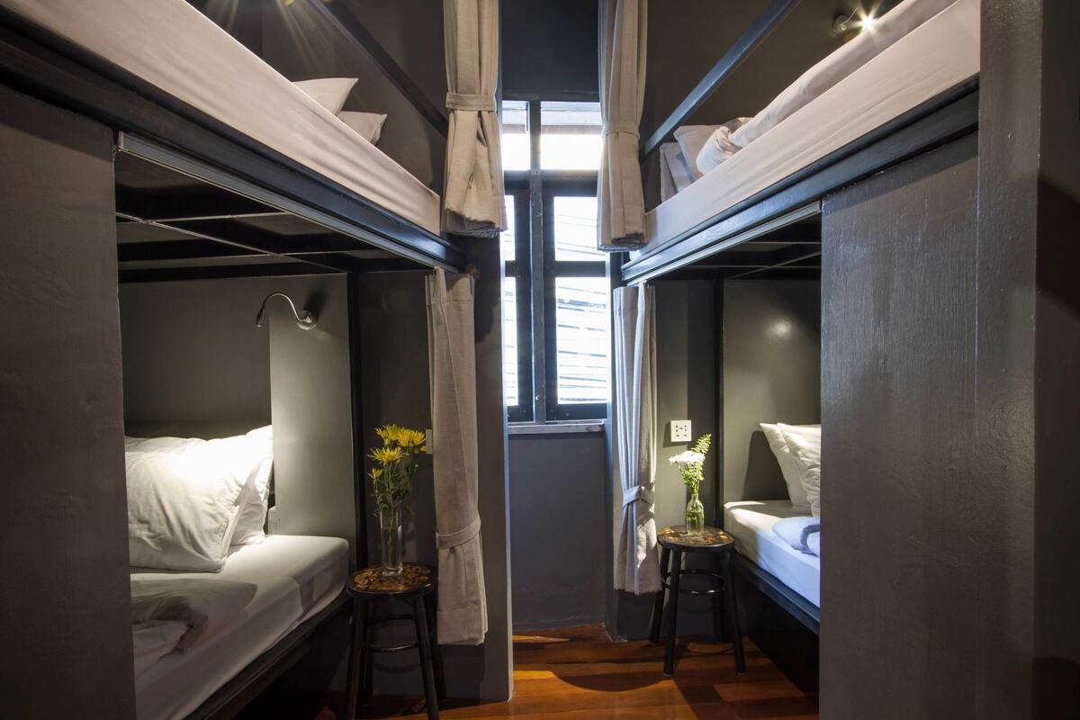 A compact room with bunk beds, a small table with a vase, and a window with curtains.