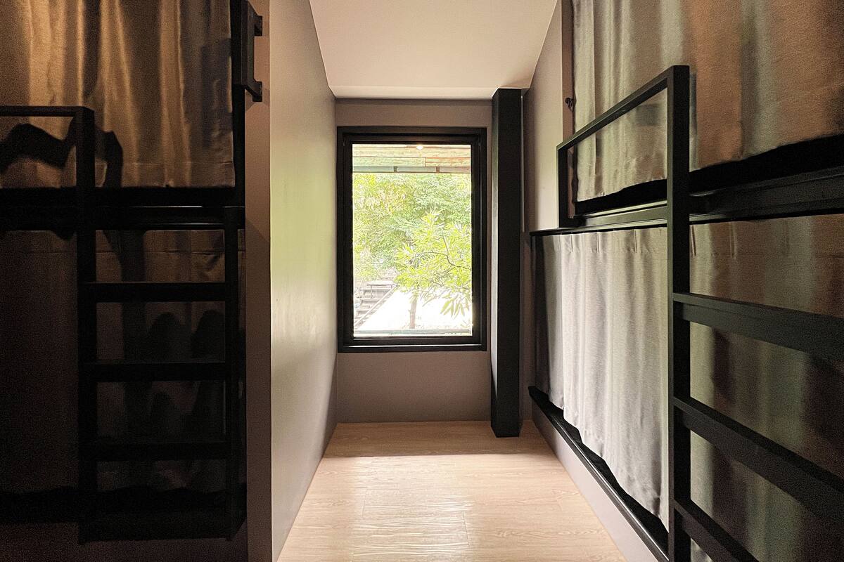 A narrow hallway with a window at the end, wooden flooring, and a metal gate on the left.