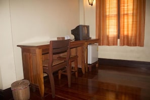 Una habitación con un escritorio de madera, dos sillas, un televisor y un refrigerador.