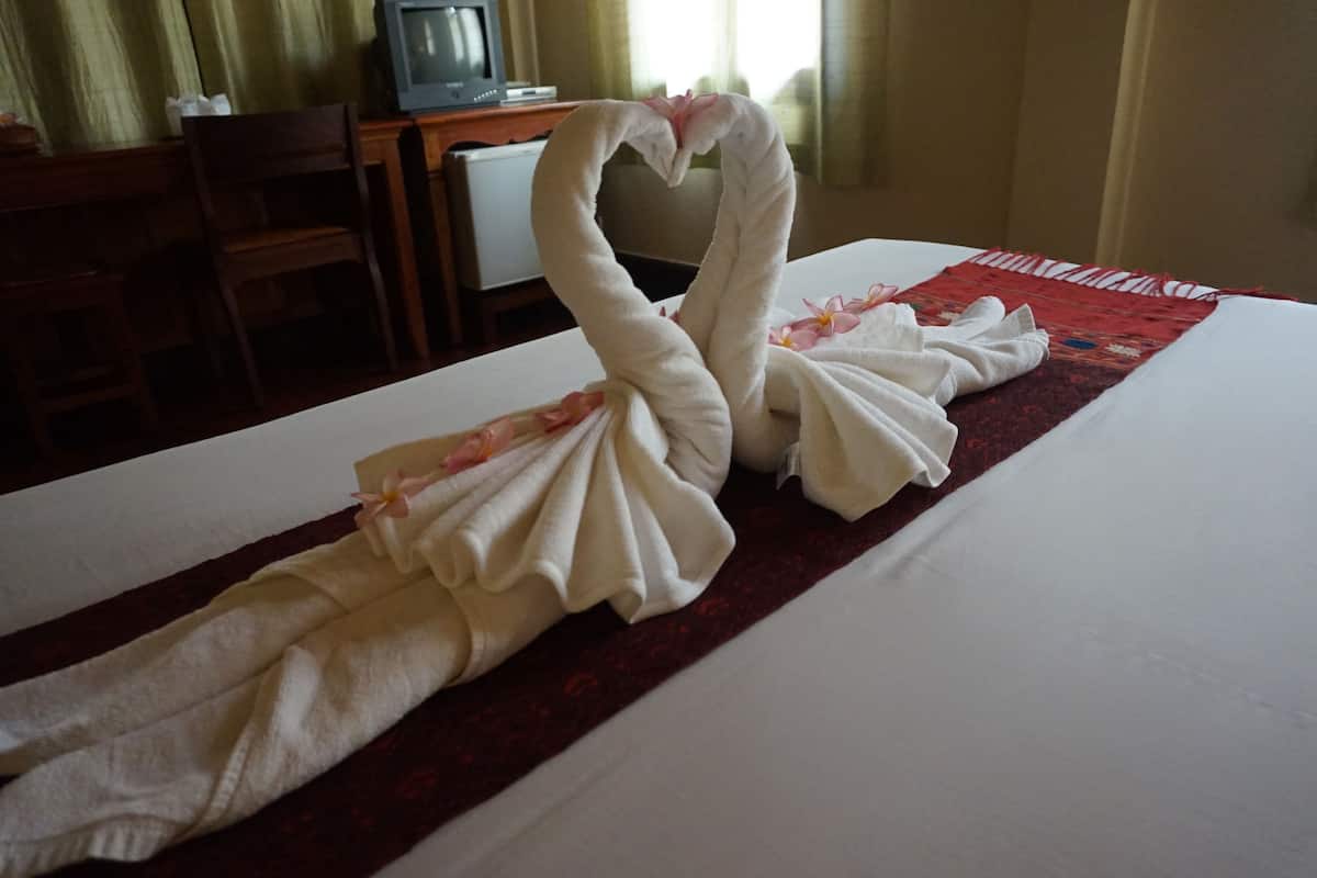 Habitación de hotel con una cama decorada con dos toallas con forma de cisne y una manta roja.