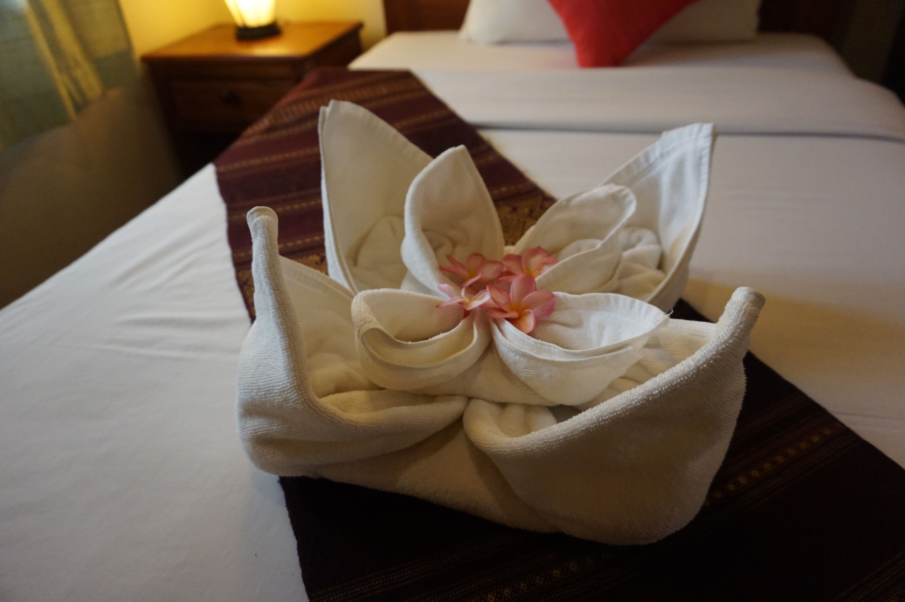Une serviette soigneusement pliée, ornée d’une fleur, est posée sur le lit.