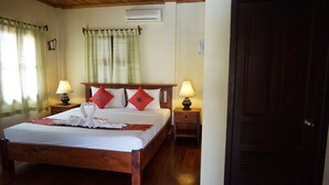 Una cama bien hecha con edredón blanco y almohadas rojas, dos lámparas de noche, cabecera de madera y una puerta de madera.