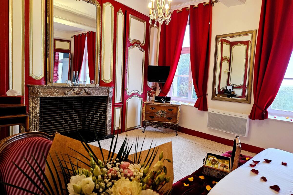 A hotel room with a fireplace, a television, a large mirror, and red curtains.