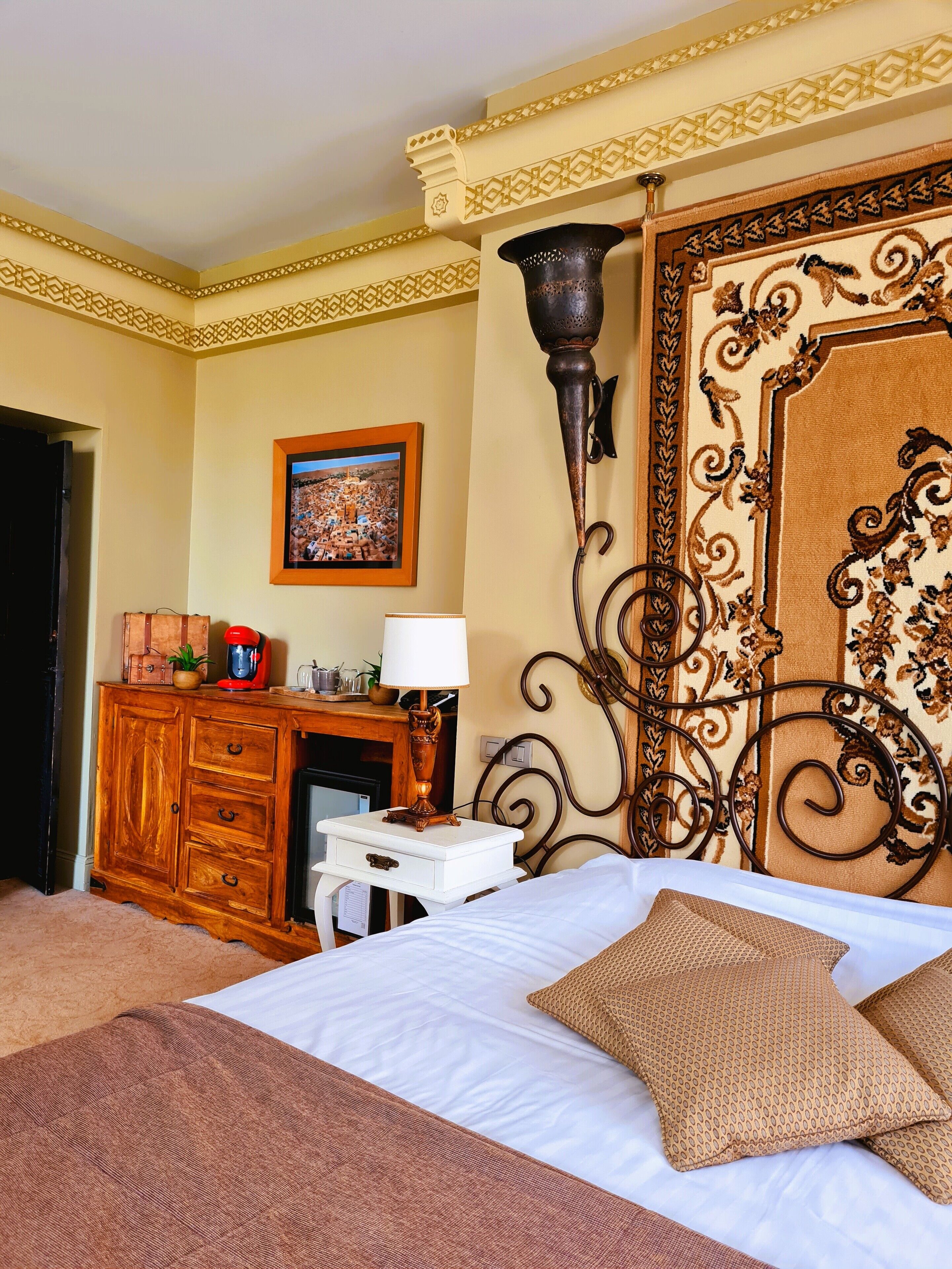 Una camera d'albergo con un letto, una scrivania con una lampada, un camino e una decorazione a parete.