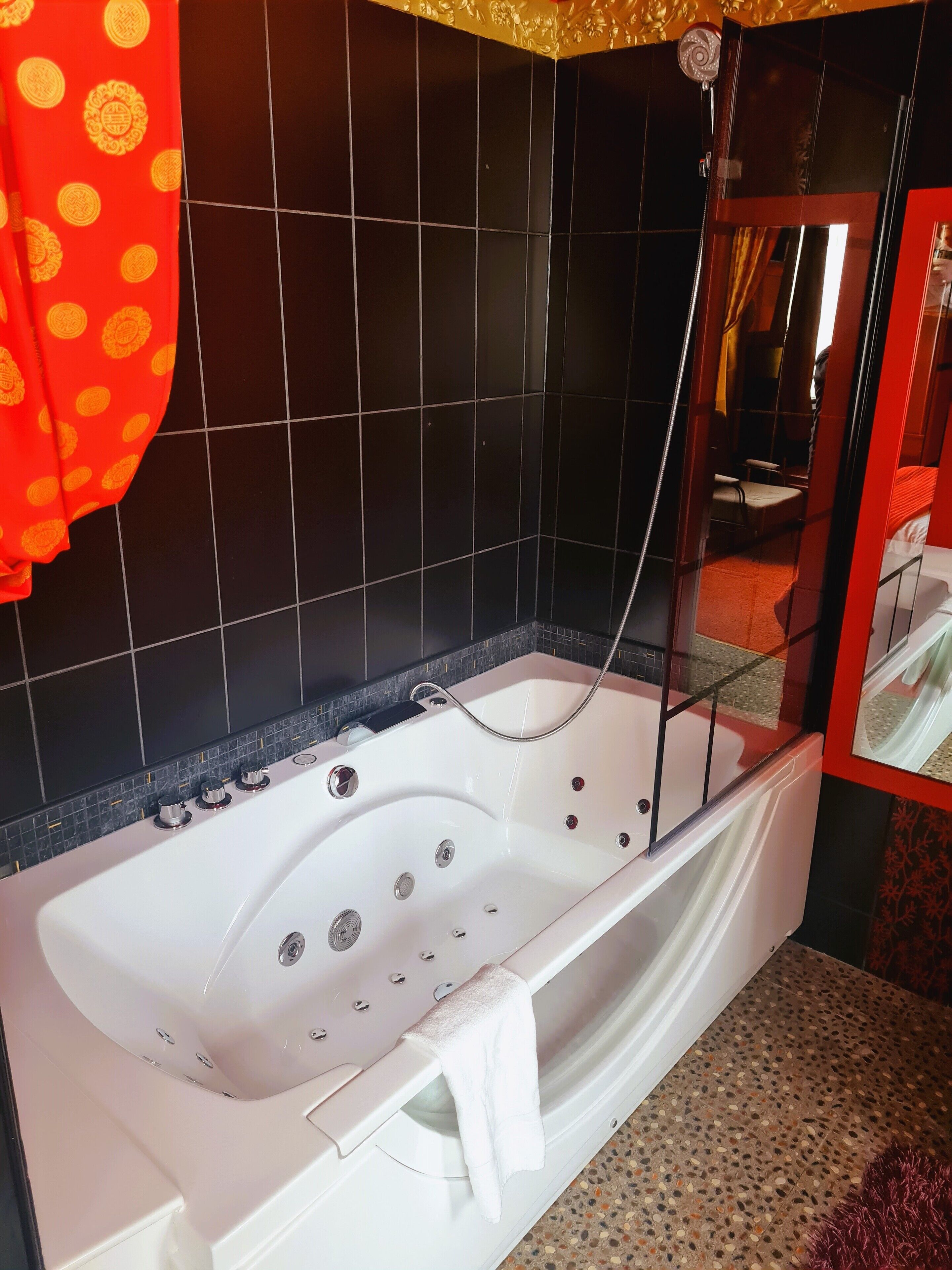 A modern bathroom with a white bathtub, black tiled walls, and a red patterned curtain.