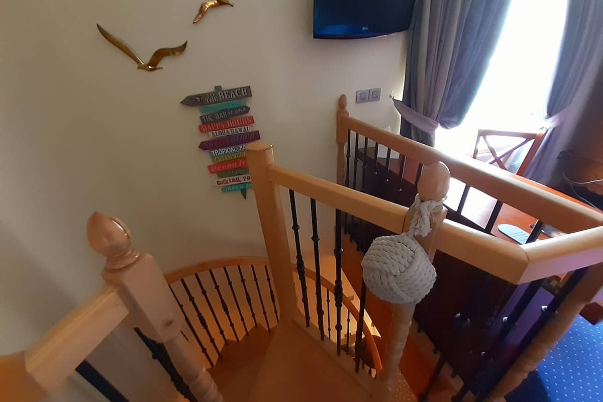 A wooden staircase with a handrail, a wall-mounted TV, and a row of colorful signs indicating various amenities.