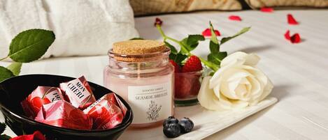Una bandeja ordenada con un tarro de vela perfumada, un cuenco de bombones, una rosa blanca y pétalos de rosa esparcidos.