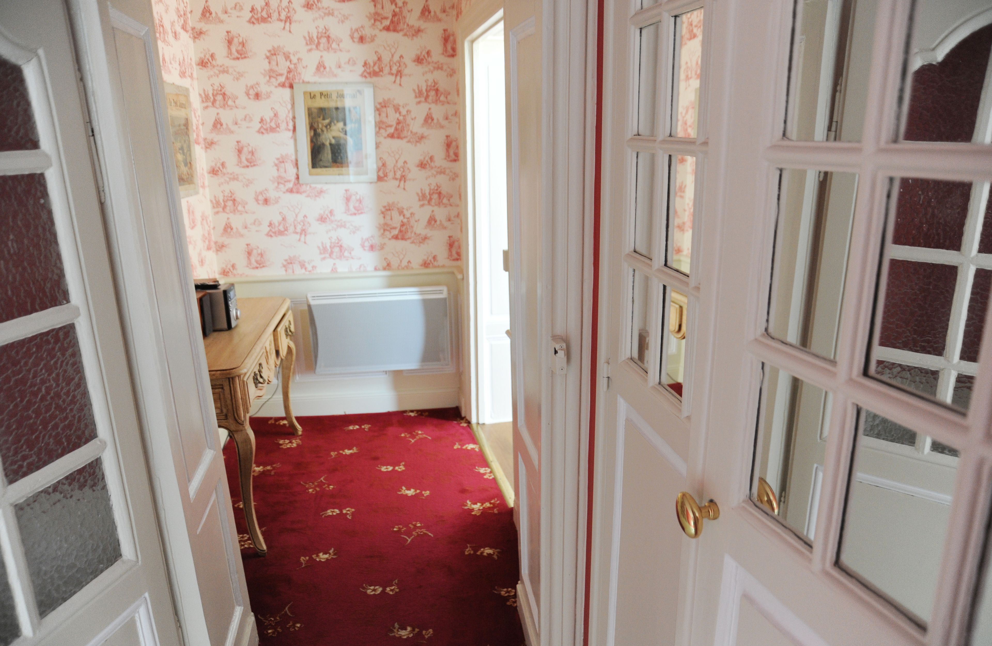 A hallway with a red carpet, a wooden dresser, and a framed picture on the wall.