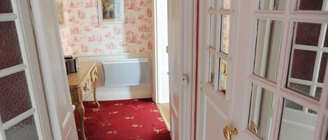 A hallway with a red carpet, a wooden dresser, and a framed picture on the wall.