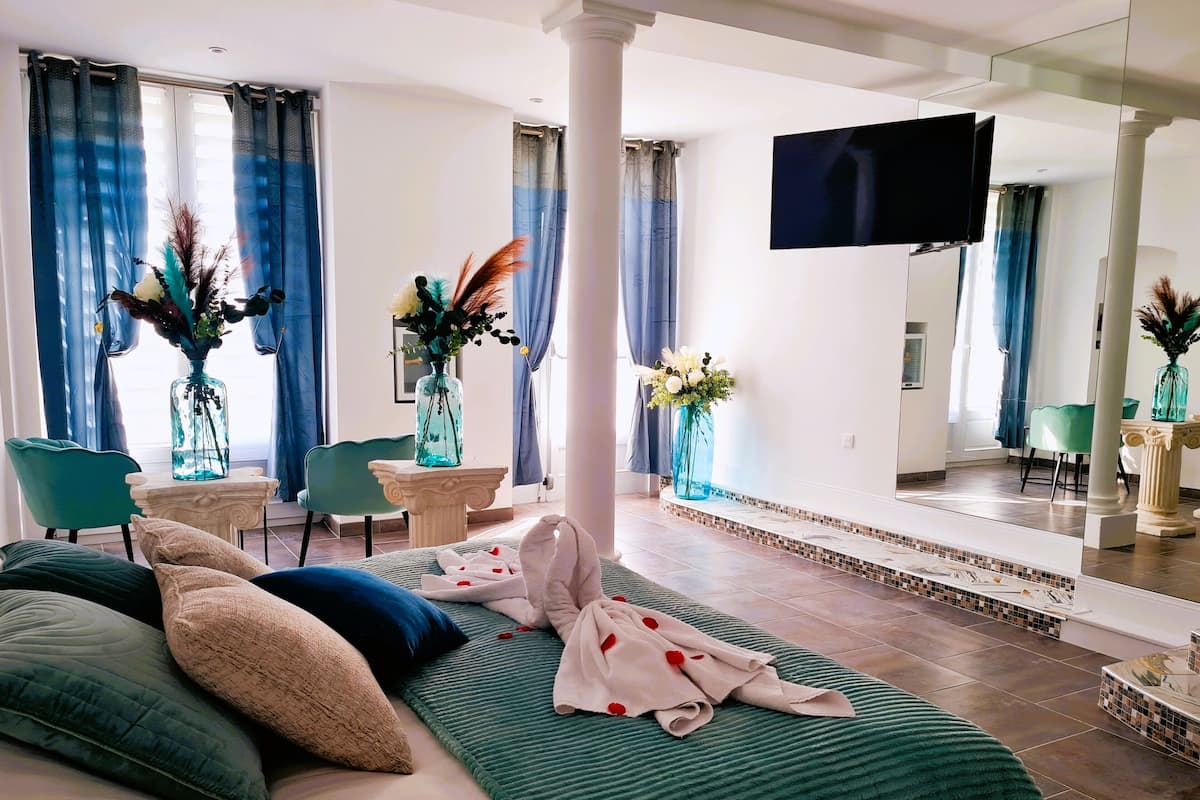 A hotel room with a bed, a TV, a dining area, and a bathroom.