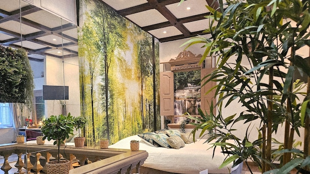 A hotel room with a large forest mural, a bed with multiple pillows, a small table with a menu, and a balcony with plants. - Châtellerie de Schoebeque (Cassel)