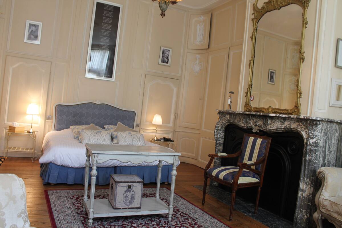 A bedroom with a large bed, a dresser, a chair, and a fireplace.