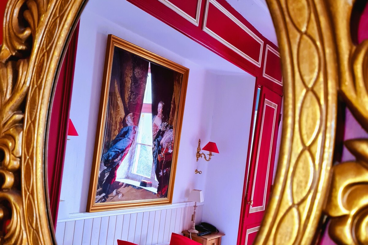 A room with a bed, a red and white color scheme, a painting on the wall, and a red lamp.