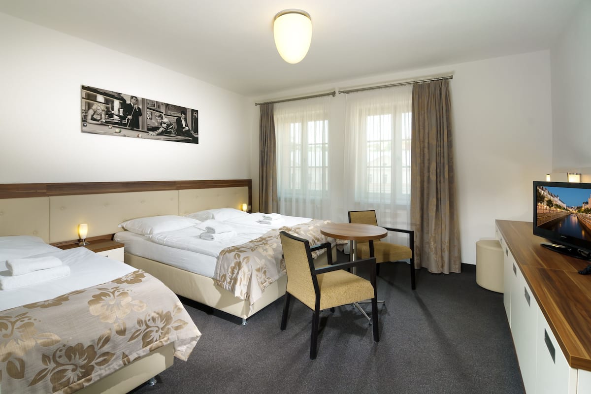 A hotel room with two beds, a dining table, chairs, a television, and a painting on the wall.