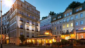 A hotel with multiple floors, outdoor seating, and a well-lit entrance. - Hotel Malta (Karlovy Vary)